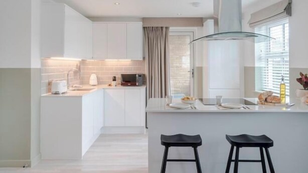 Een moderne keuken met witte kasten, een glazen kookeiland en twee zwarte barkrukken.