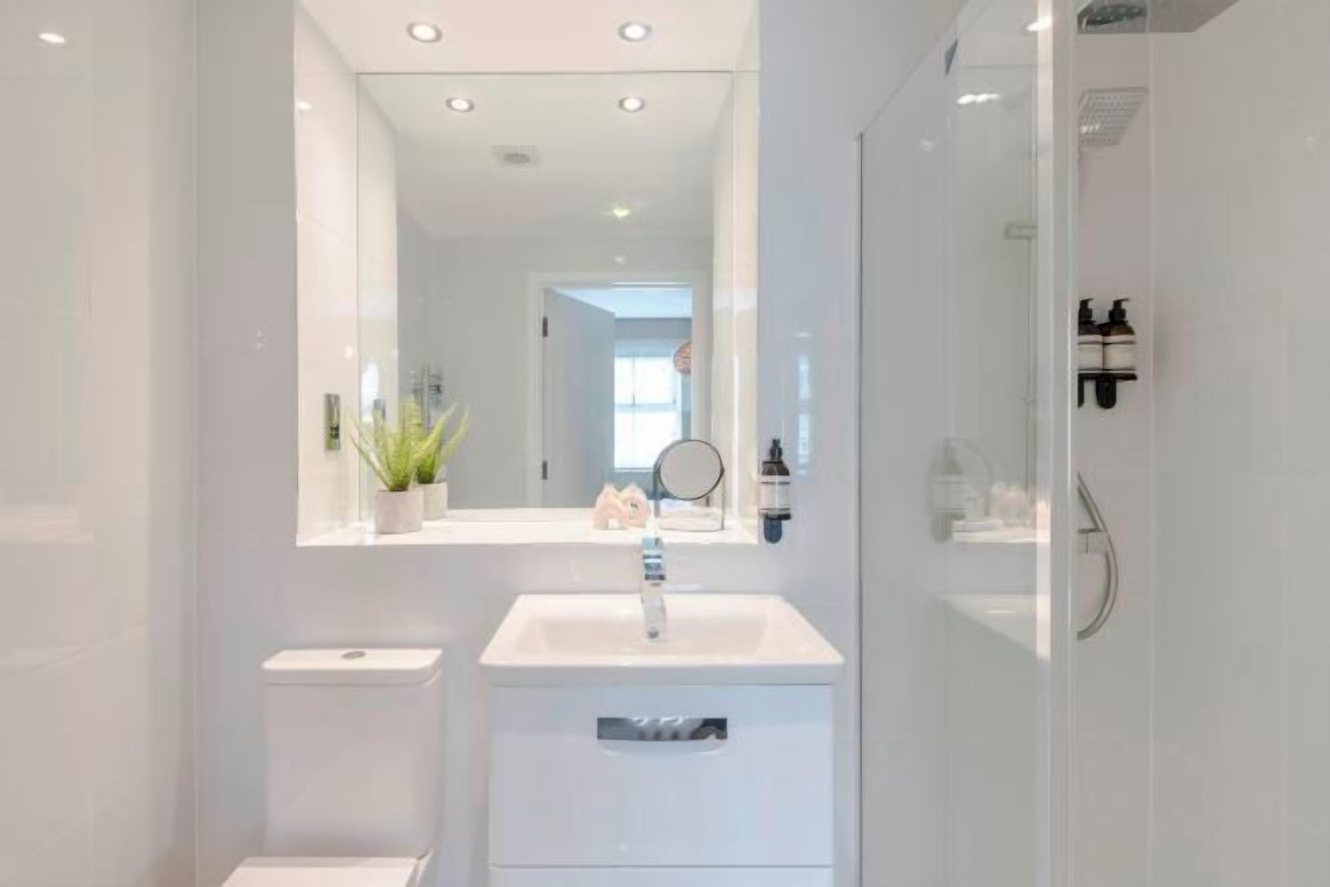 A modern bathroom with a white sink, mirror, and glass shower enclosure.