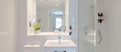 A modern bathroom with a white sink, mirror, and glass shower enclosure.