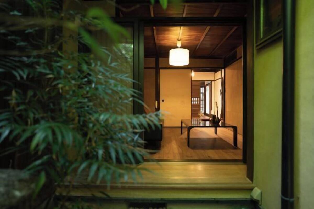A traditional Japanese interior with a wooden floor, a hanging light fixture, and a view into a room with a tatami mat.