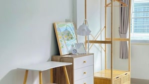 Ein Zimmer mit weißem Schreibtisch, Holzschrank, Kleiderstange und einem Fenster mit Vorhängen.