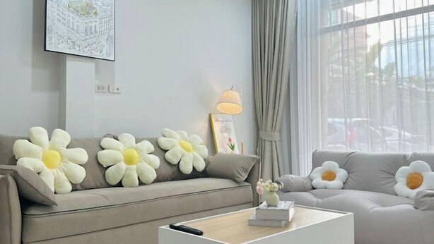 Ein modernes Wohnzimmer mit einem beigen Sofa, großen, blumenförmigen Kissen, einem weißen Couchtisch und einem gerahmten Bild an der Wand.