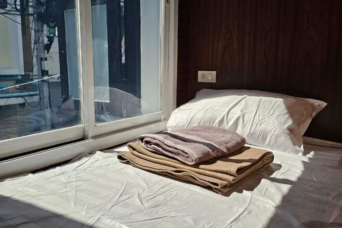 A bed with a white sheet and a rolled-up towel, a white pillow, and a window with a view of the outside.