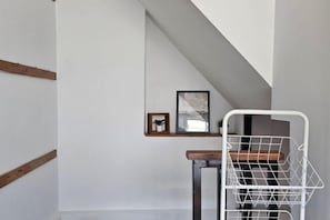A room with a sloped ceiling, a white wall, a wooden beam, a metal rack, and a small shelf with framed pictures. - Seen Hostel Bangkok The Riverwalk (Bangkok)