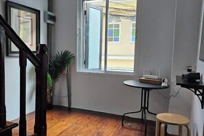 A room with a wooden floor, a window with a view, a small table with a chair, and a staircase. - Seen Hostel Bangkok The Riverwalk (Bangkok)