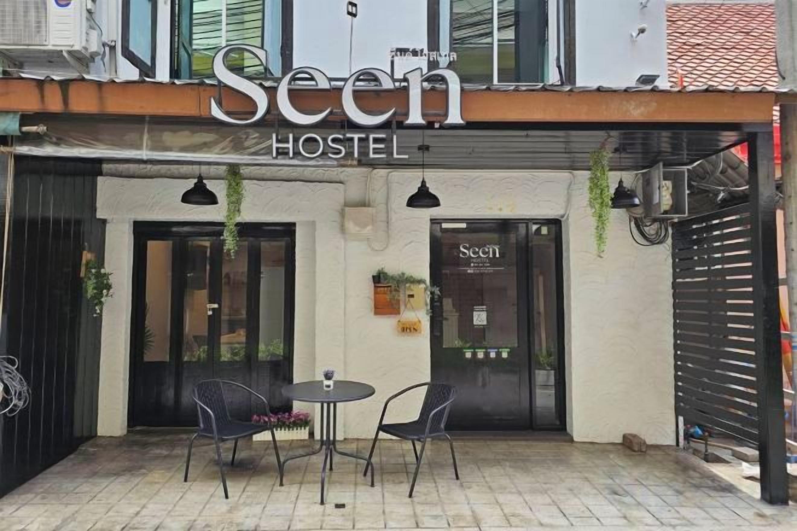 Une auberge de jeunesse appelée « Seen », avec une enseigne au-dessus de l’entrée, deux tables avec des chaises à l’extérieur et une entrée fermée par un portail.