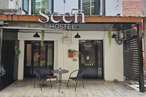 A hostel named 'Seen' with a sign above the entrance, two tables with chairs outside, and a gated entrance. - Seen Hostel Bangkok The Riverwalk (Bangkok)