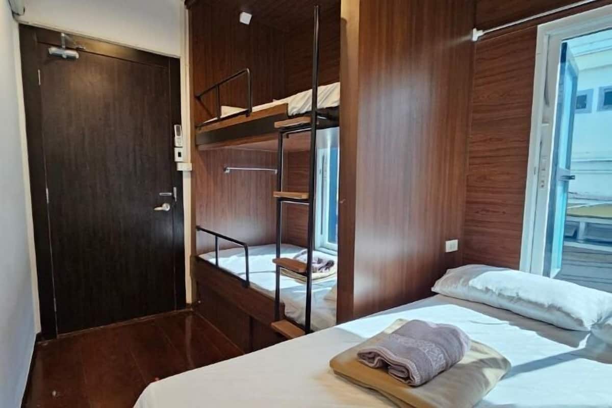 A room with a bunk bed, a single bed, a wooden door, and a window.