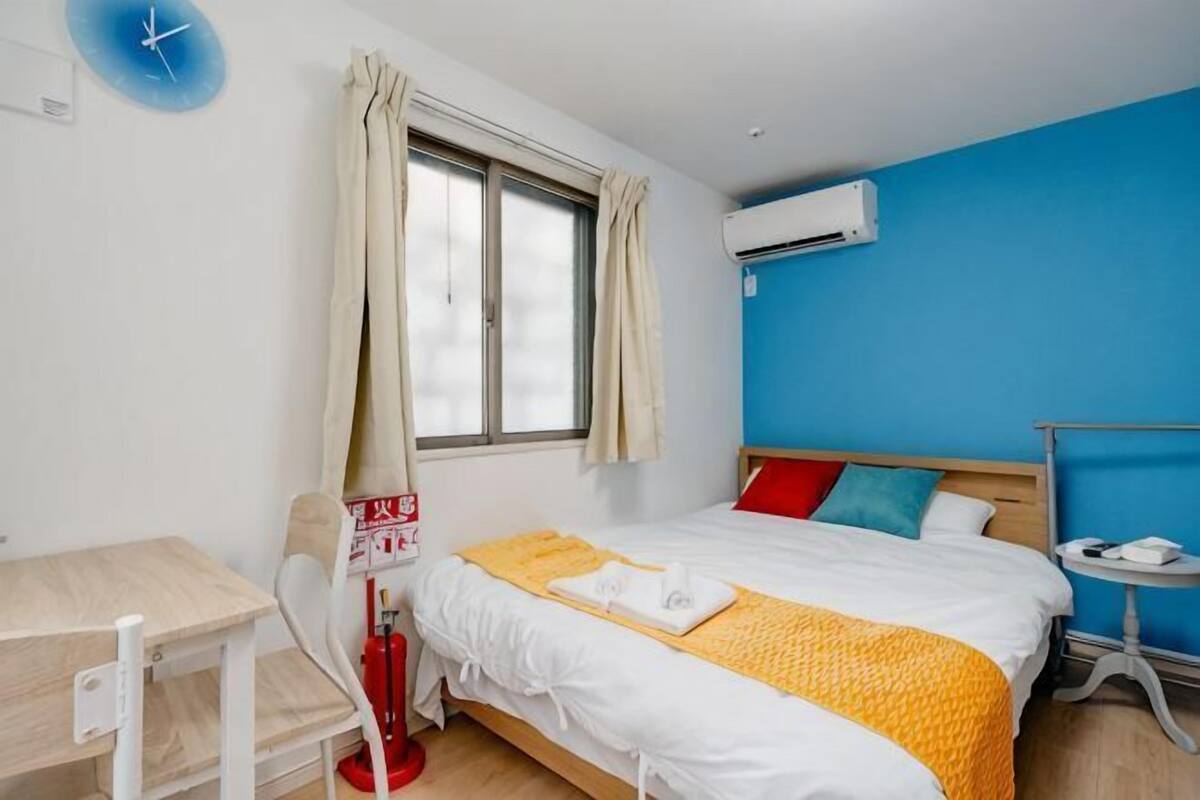 A hotel room with a bed, a desk, a chair, a window with curtains, and an air conditioning unit.