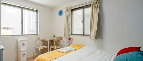 A bedroom with a bed, a desk, a chair, a window, and a wall clock.