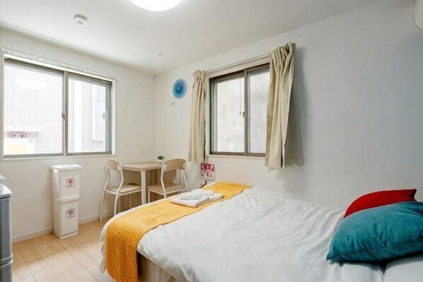 A bedroom with a bed, a desk, a chair, a window, and a wall clock.