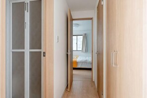 Un pasillo estrecho que conduce a un dormitorio con una cama, un ventanal y una puerta.