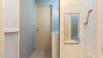 A narrow hallway leading to a door, a shower area with a handheld showerhead, and a mirror on the wall.