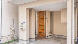 A modern entrance with a wooden door, a small step leading inside, and a utility box on the wall. - CROWN OOJIMA (Tokyo)