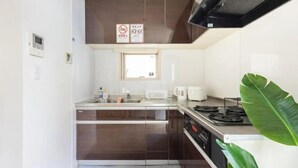 A compact kitchen with dark cabinets, a window, a stove, and a coffee maker. - CROWN OOJIMA (Tokyo)