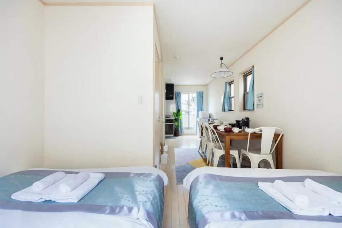 A hotel room with two beds, a dining table with chairs, and a kitchenette in the background.