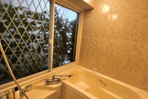 A bathroom with a bathtub, a window with a view of trees, and a towel rack. - CROWN OOJIMA (Tokyo)