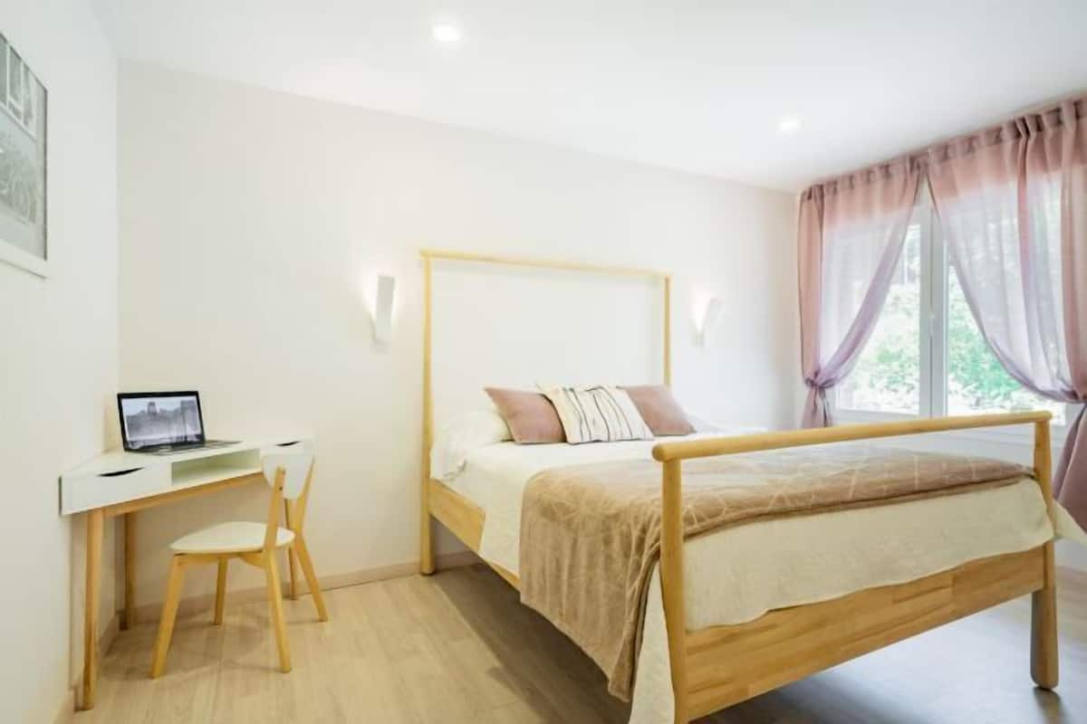 Un dormitorio con una cama de madera, un escritorio con una computadora portátil y una silla.