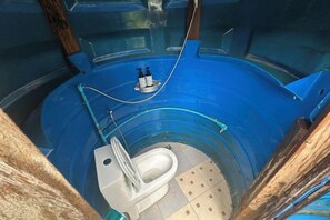 Un baño circular con inodoro blanco, suelo azul y un lavamanos pequeño.