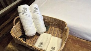 Een rieten mand met twee witte handdoeken en een opgevouwen handdoek op een bed.