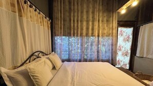 Een net opgemaakt bed met witte lakens, een hoofdbord en een raam met gordijnen.