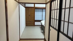 Egy hagyományos, japán stílusú szoba, tatami szőnyeggel, tolóajtóval és fehér ágyneművel ellátott ággyal.