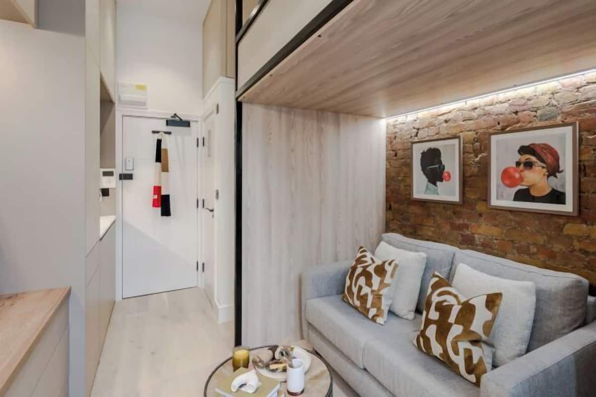 A modern living room with a grey sofa, patterned cushions, a coffee table with books and a cup, and a stone wall with framed artwork.