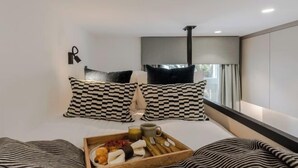 A modern hotel room with a bed, checkered pillows, a tray with breakfast items, and a window with curtains. - Kensington The Loft (London)