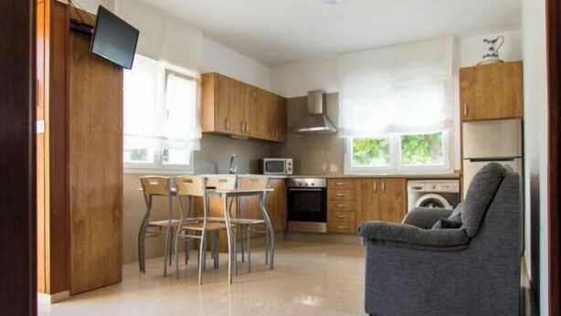 Eine moderne Küche mit Holzschränken, einem Essbereich mit Stühlen, einem grauen Sofa und einem an der Wand befestigten Flachbildfernseher.