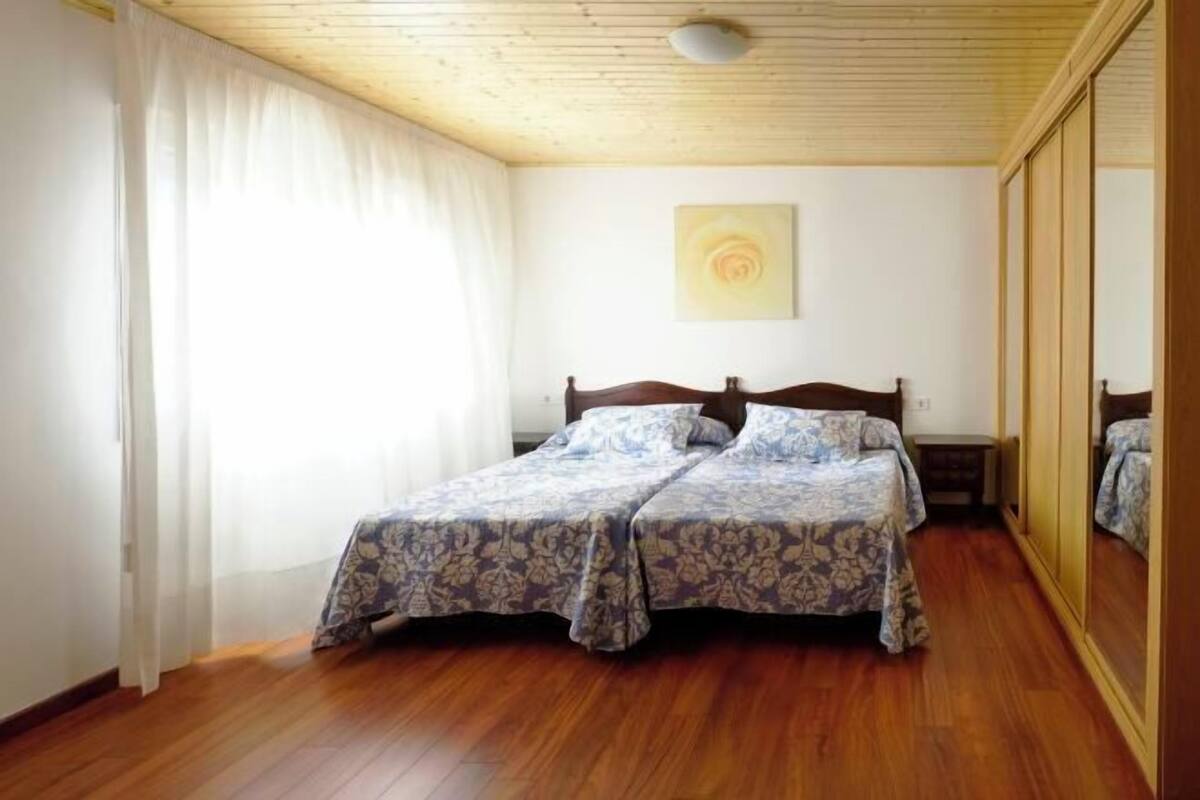 Une chambre avec un plafond en bois, un lit recouvert d’une literie à motifs floraux, un miroir et un tableau accroché au mur.