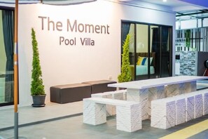 A reception area with a sign reading 'The Moment Pool Villa,' a reception desk, seating area, and a potted plant. - The Moment Pool Villa (Sattahip)