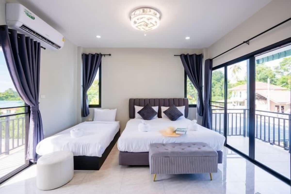 A hotel room with a large bed, a small table, a bench, and a balcony with a view.