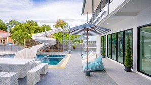 A modern outdoor pool area with a spiral slide, lounge seating, and umbrellas. - The Moment Pool Villa (Sattahip)