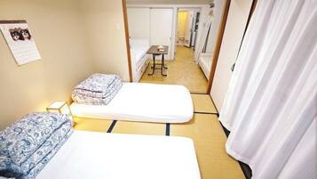 A hotel room with two beds, a small table, a calendar on the wall, and a view into the hallway.