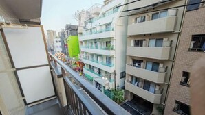 A balcony with a view of multi-story buildings, a green flag, and a whiteboard. - SUMMERSONG (Tokyo)