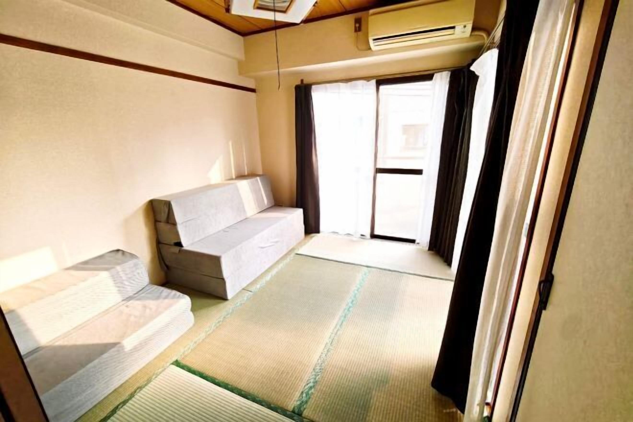 A room with tatami flooring, a sofa, a sliding door, and an air conditioning unit.