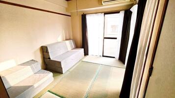 A room with tatami flooring, a sofa, a sliding door, and an air conditioning unit.