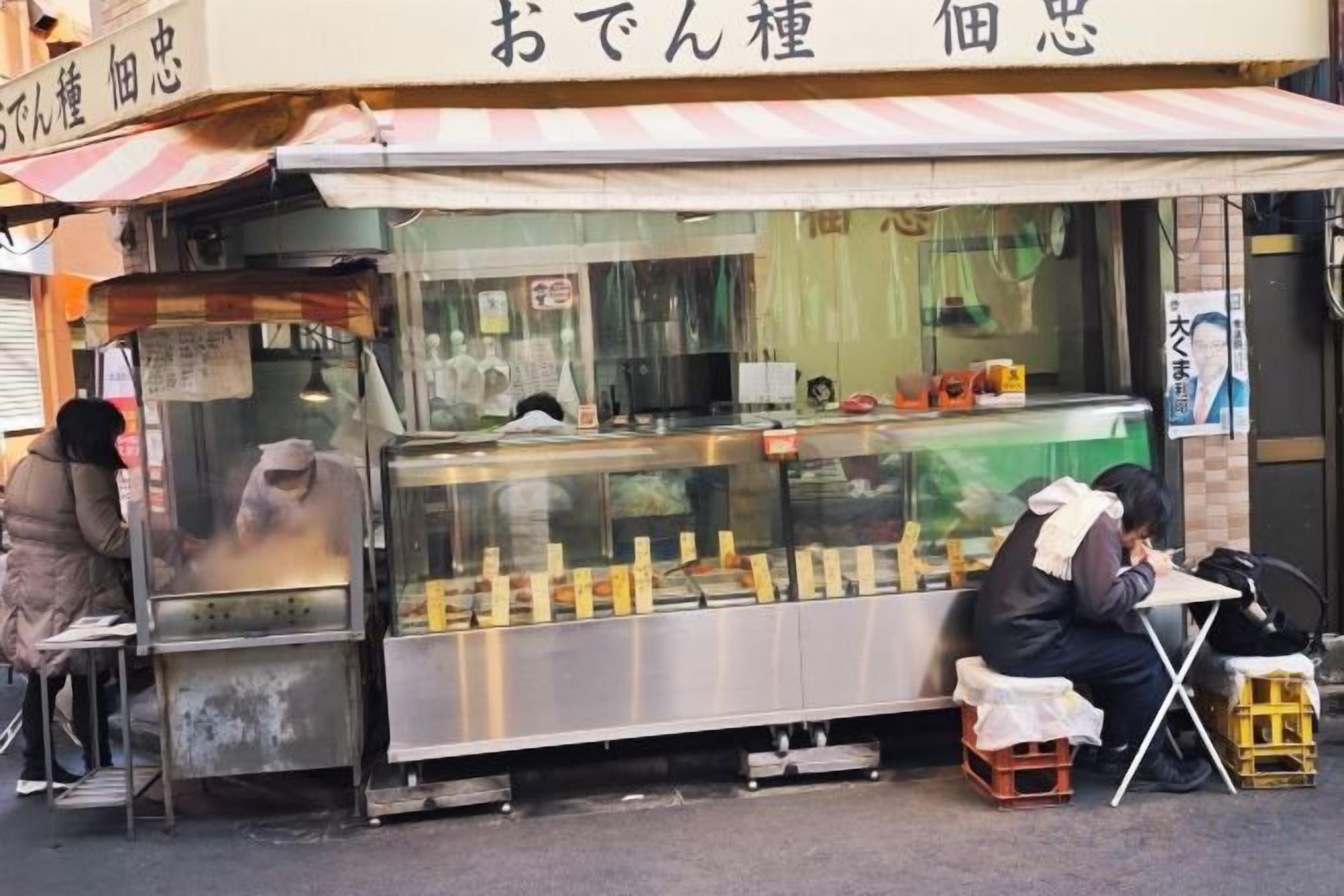 A street food stall with a metal counter and a person sitting at a table.