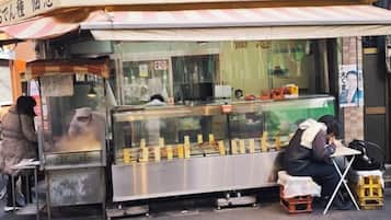 A street food stall with a metal counter and a person sitting at a table.
