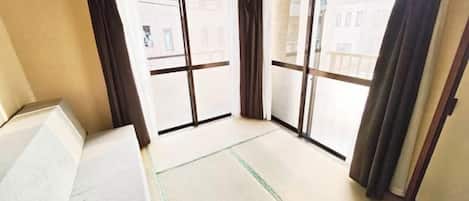 A room with tatami flooring, sliding doors, and a view of buildings outside.