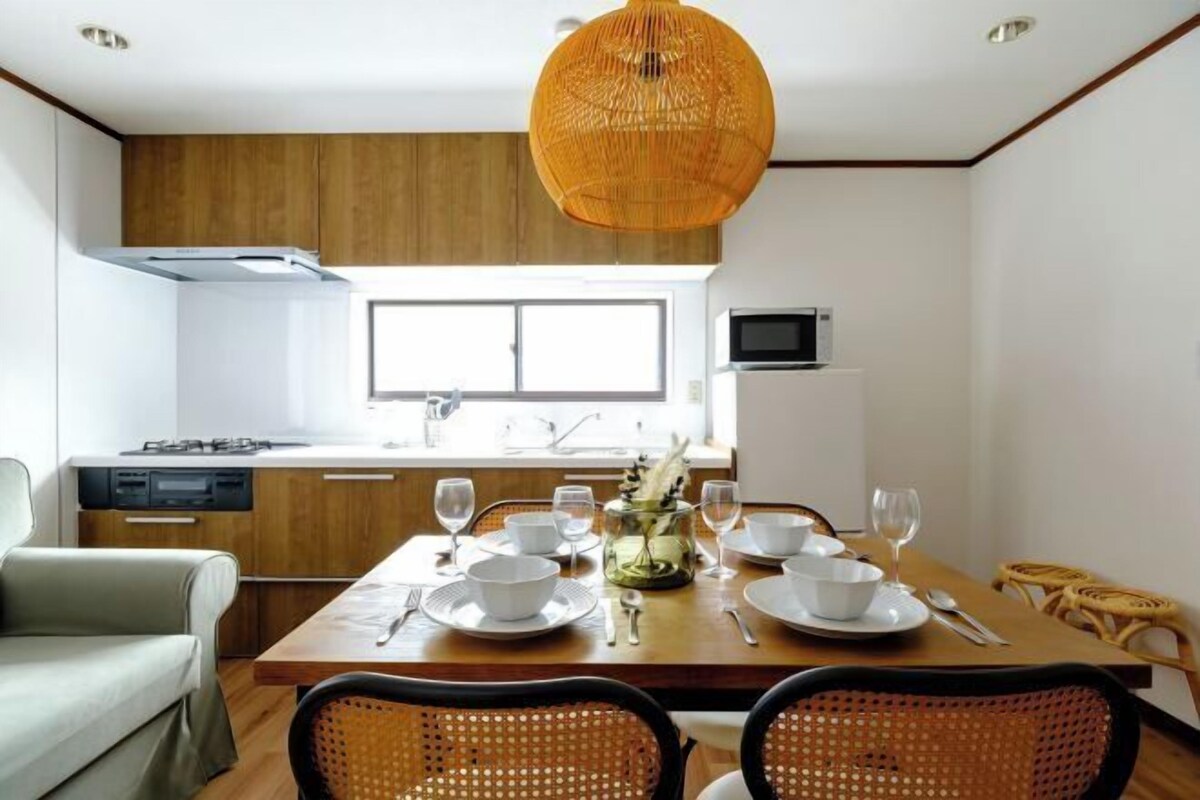 Una cocina moderna con armarios de madera, una mesa de comedor preparada para cuatro personas y una lámpara colgante de fibras naturales.
