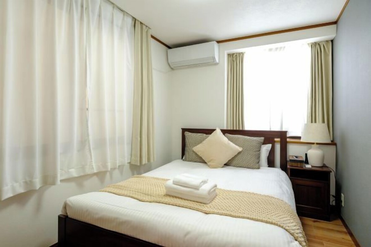 A hotel room with a bed, curtains, a nightstand, and a window.