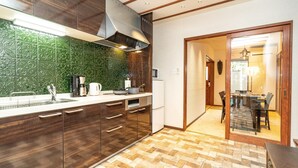 A kitchen with a green patterned backsplash, wooden cabinets, a microwave, and a dining area with a table and chairs. - Kyobu Higashiyama (Kyoto)