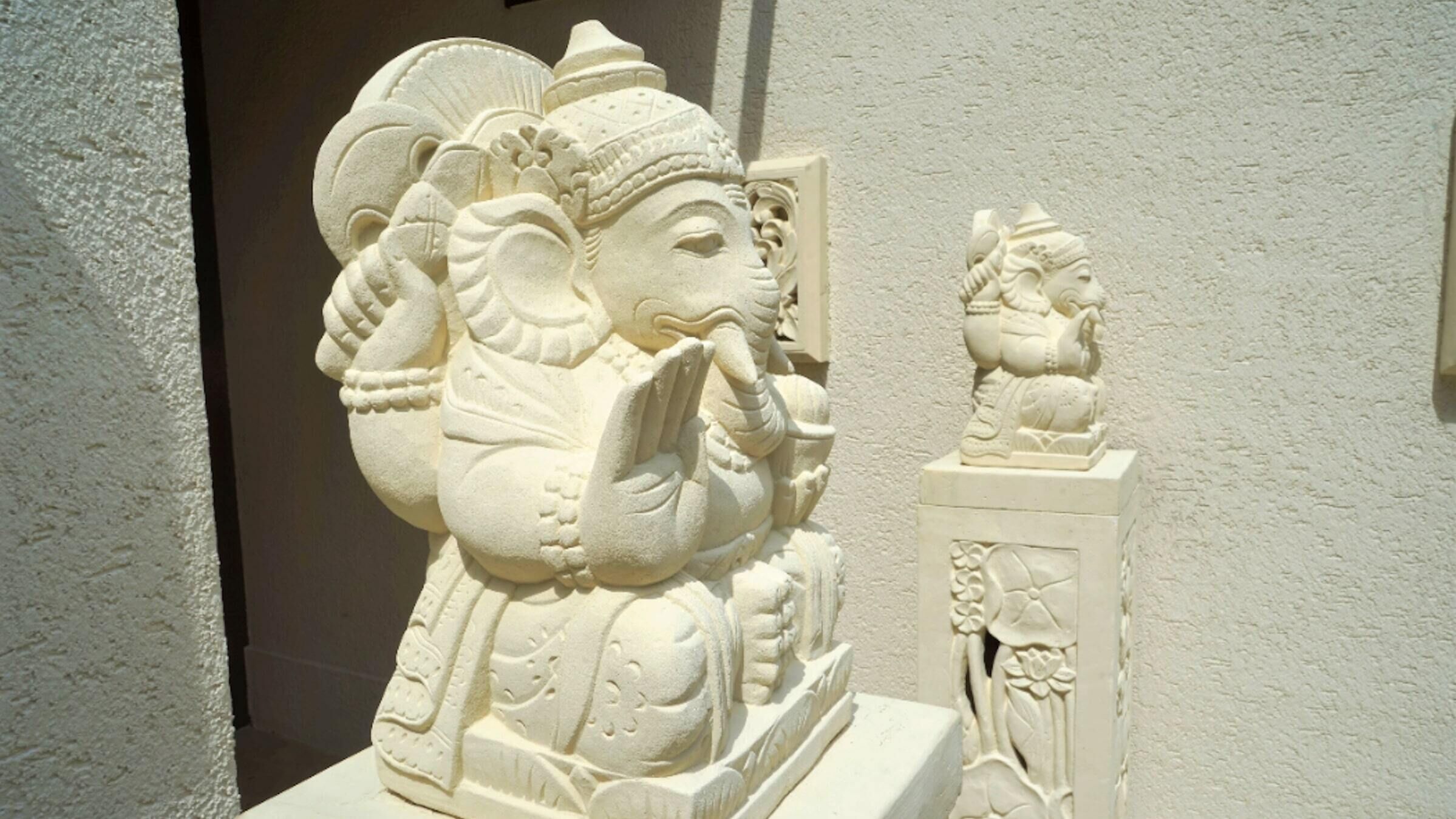 A white stone sculpture of a deity with a large head, elaborate headdress, and a small figure beside it.