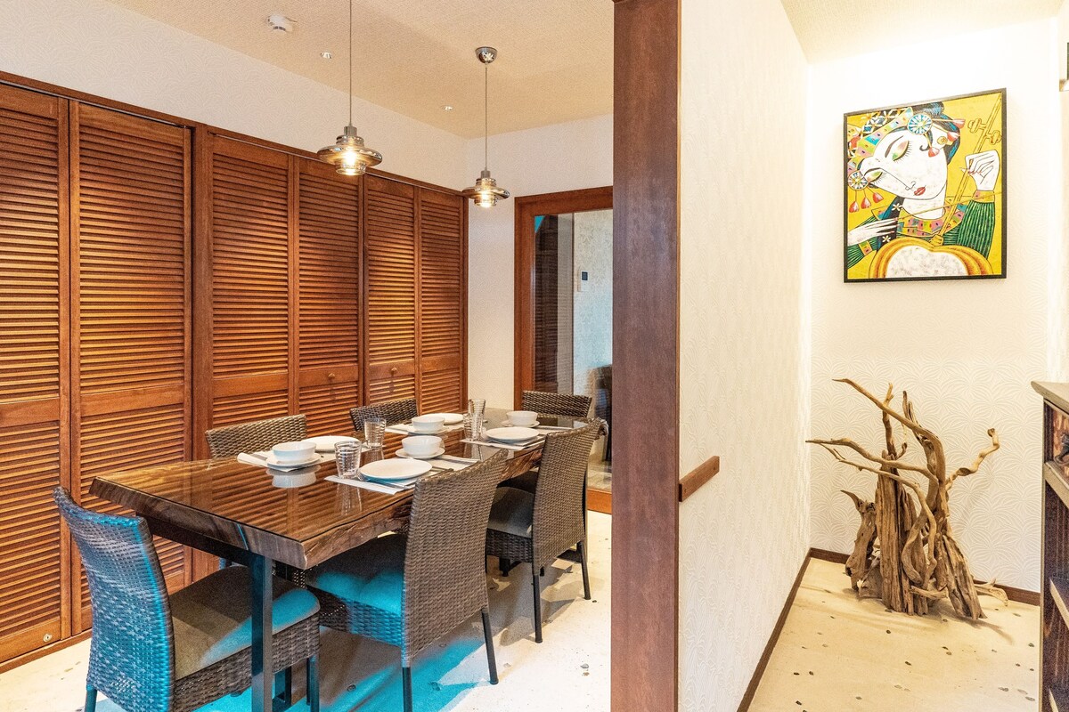 A dining area with a wooden table, wicker chairs, and a painting on the wall.