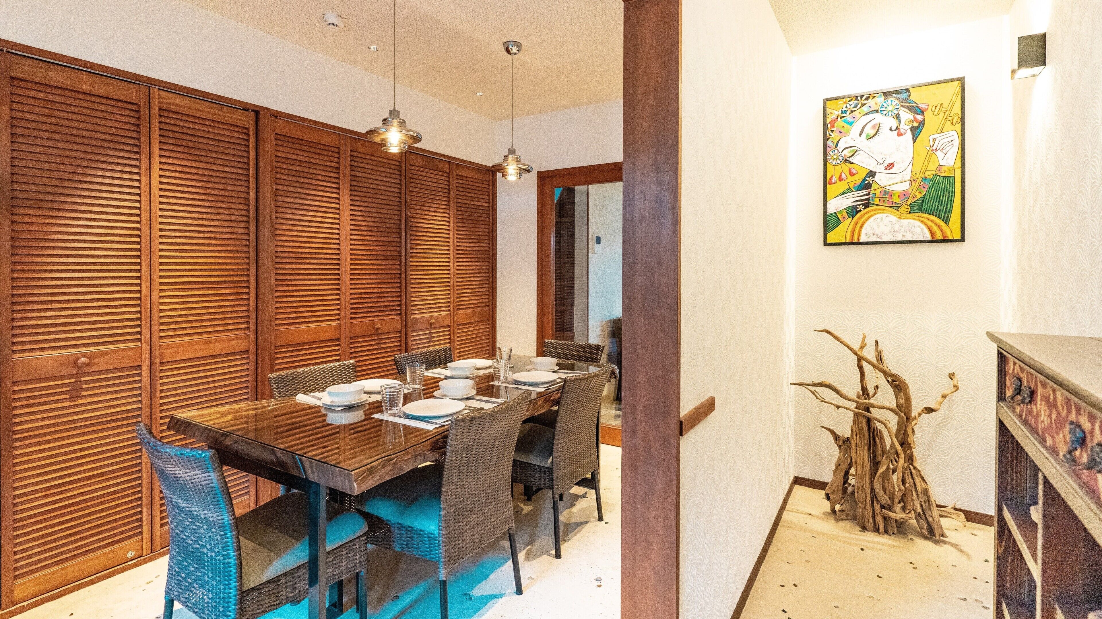A dining area with a wooden table, wicker chairs, and a painting on the wall.