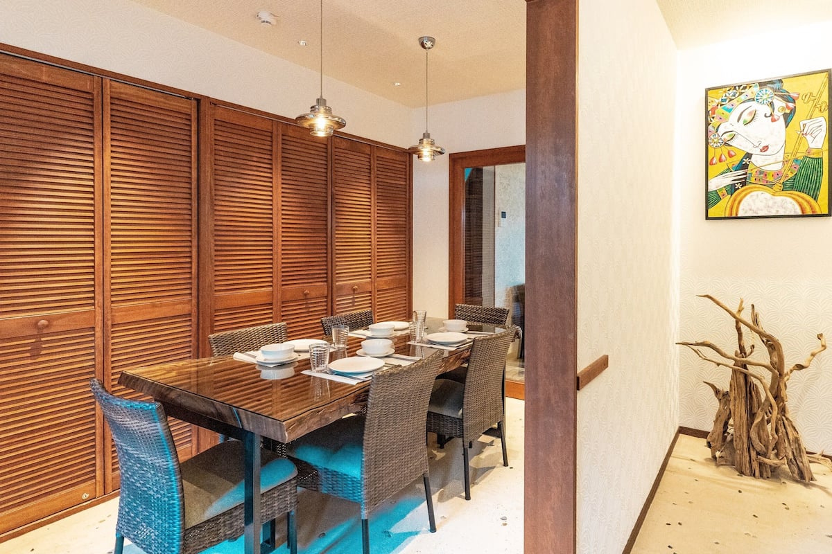A dining area with a wooden table, wicker chairs, and a painting on the wall.