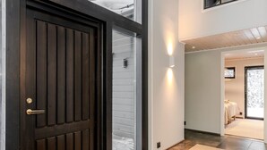 Un intérieur moderne avec une porte en bois foncé, un couloir menant à une chambre à coucher équipée d’un lit et d’une fenêtre.