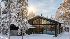 Une cabane moderne aux grandes fenêtres, entourée d’arbres couverts de neige.