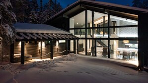 Une maison moderne avec une façade en verre, un patio couvert et un paysage enneigé.